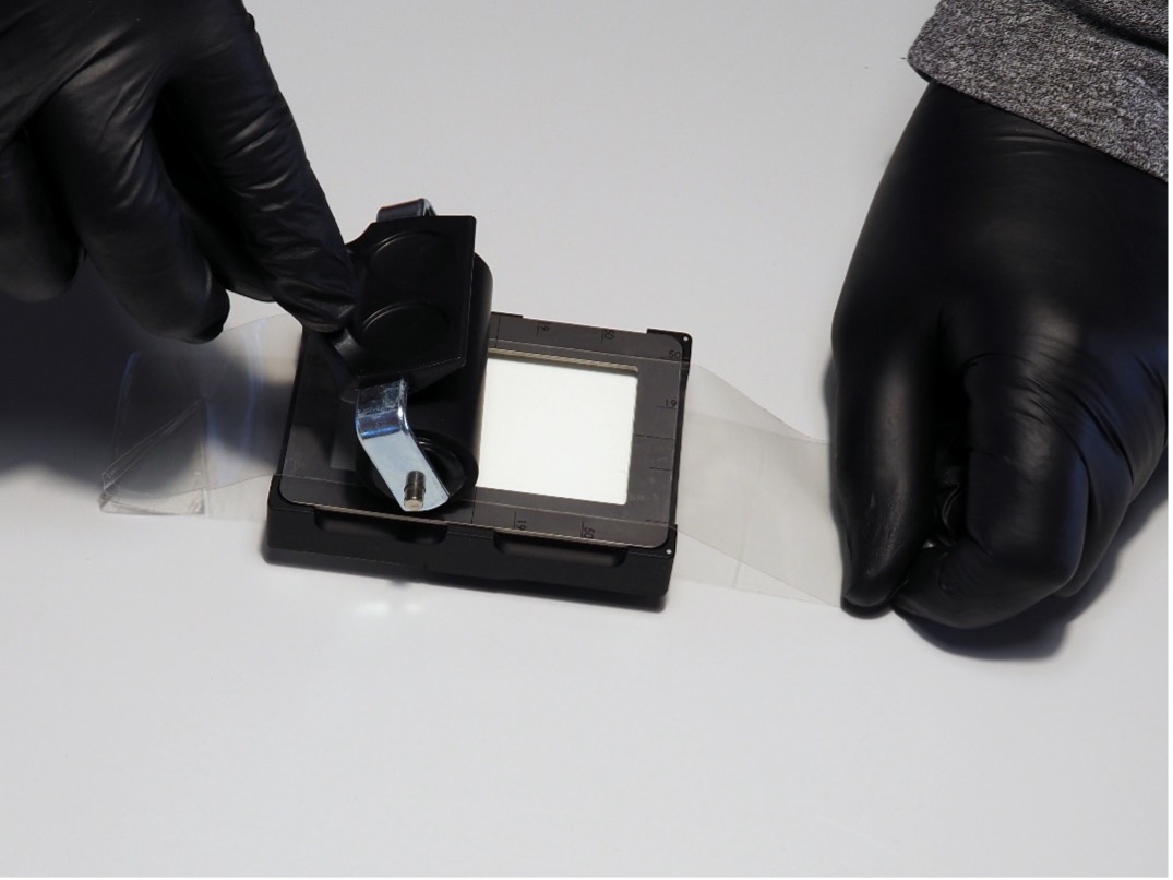 Přitisknutí pásky se vzorkem k držáku vzorků odebraných páskou pomocí pryžového válečku