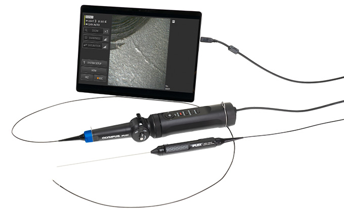 Tablet displaying an image of the inside an engine beside an IPLEX TX II ultraslim video borescope with rigid and flexible small diameter insertion tubes laying on a table. 