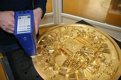 Moneda de oro de 24 quilates de peso pesado siendo analizada mediante espectroscopia de rayos X con un analizador XRF.