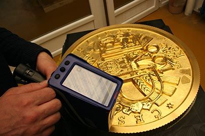 Анализатор-пистолет, измеряющий содержание золота в большой золотой монете на монетном дворе, где она была произведена