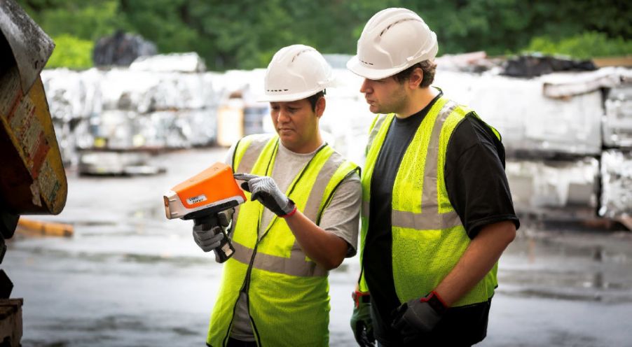 Recycling industry workers using an XRF analyzer to sort metal at a scrap yard